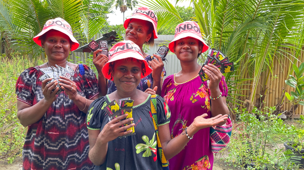 Four women in bright pick hats holding condoms up to the camera.