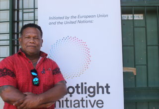 A man in a red shirt stands in front of a banner that reads 'Spotlight Initiative'.