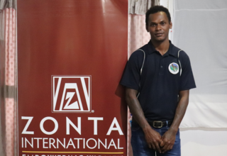 Young man in dark shirt stands in front of banner reading 'Zonta International'