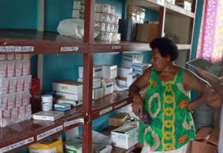 Woman in green shirt with shelves filled with medicine.