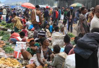 A roadside vegetable market, crowded with people.