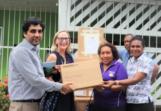 Four people hold cardboard box in from of Port Moresby General Hospital.