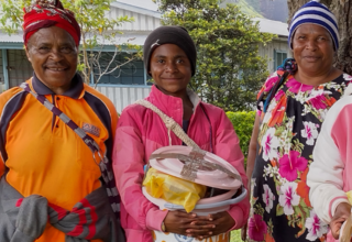 Three women stand side by side with one holding bucket with menstrual hygiene supplies.