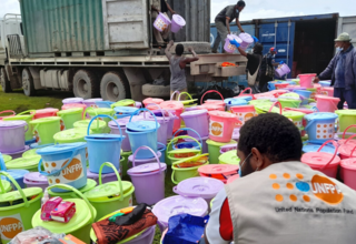 A man in a UNFPA vest packs bright buckets with sanitary supplies.