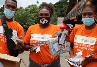 Three young people in orange with condoms and sexual health information pamphlets in market.