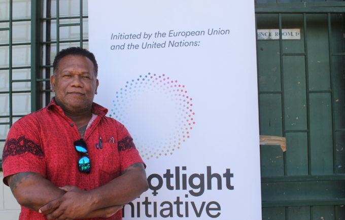 A man in a red shirt stands in front of a banner that reads 'Spotlight Initiative'.