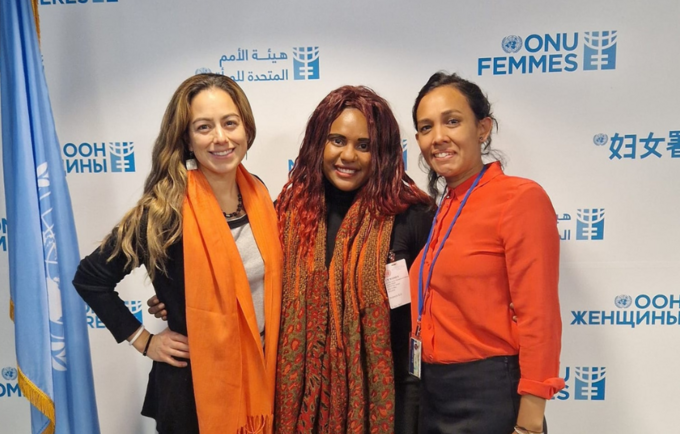 Three women stand in front of blue and white UN Women backdrop.