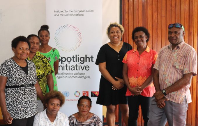 Seven people stand in front of standing banner reading ' Spotlight Initiative'.