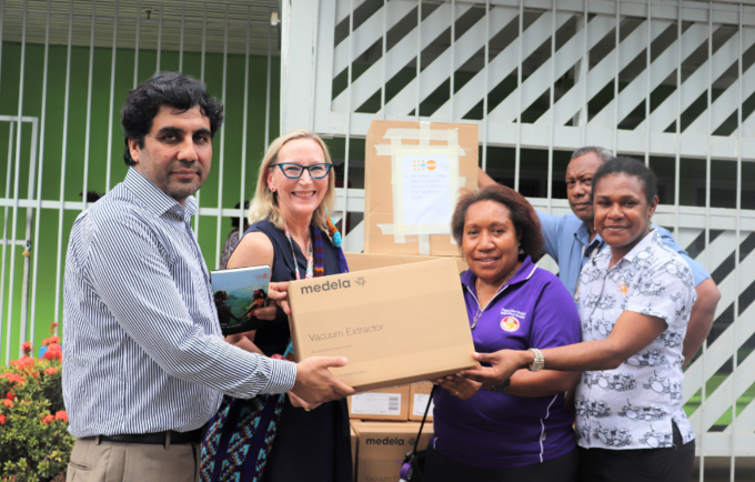 Four people hold cardboard box in from of Port Moresby General Hospital.