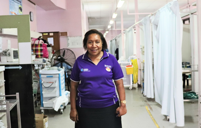A woman in a purple shirt stands in a hospital ward.