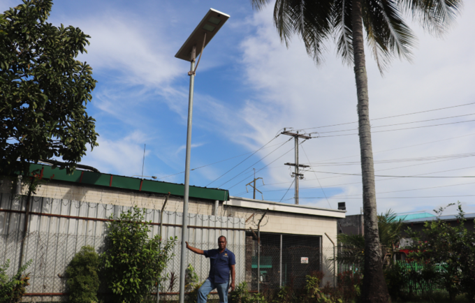 Man standing next to light pole with solar panel on top. 