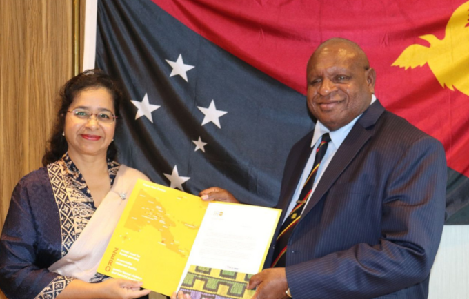 Woman and man holding folder with Papua New Guinea flag in background,