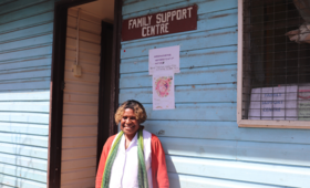 A woman in red jacket stands outside hospital ward with sign 'Family Support Centre'.