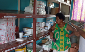 Woman in green shirt with shelves filled with medicine.