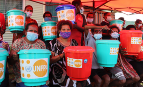 Women sit holding coloured buckets containing essential hygiene supplies.