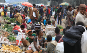 A roadside vegetable market, crowded with people.