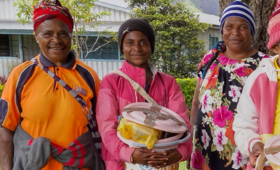 Three women stand side by side with one holding bucket with menstrual hygiene supplies.