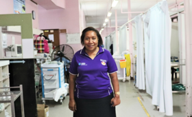 A woman in a purple shirt stands in a hospital ward.