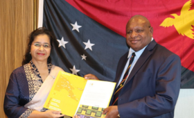 Woman and man holding folder with Papua New Guinea flag in background,