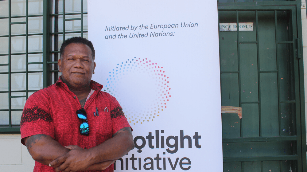 A man in a red shirt stands in front of a banner that reads 'Spotlight Initiative'.