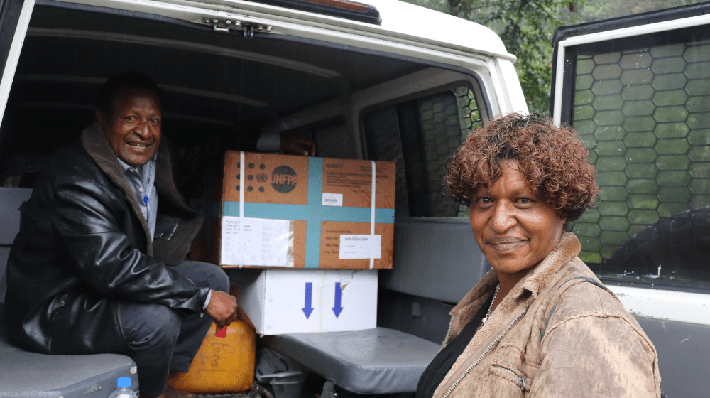 A woman stands in front of an open SUV with boxes packed inside.