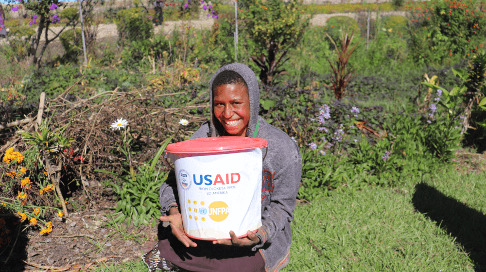 A girl in a grey hoodie holds a pink bucket.