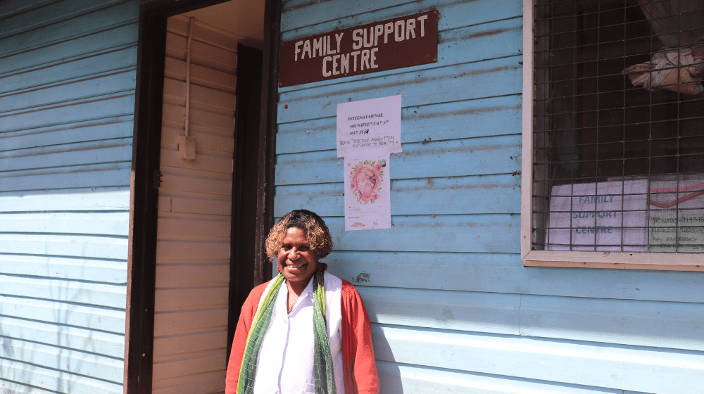 A woman in red jacket stands outside hospital ward with sign 'Family Support Centre'.