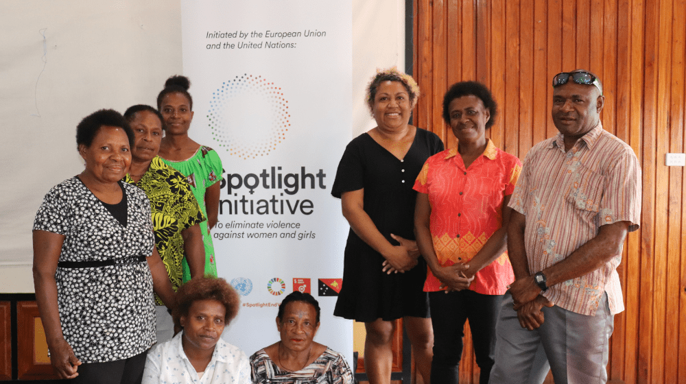 Seven people stand in front of standing banner reading ' Spotlight Initiative'.