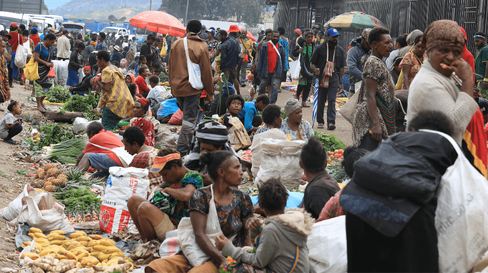 A roadside vegetable market, crowded with people.