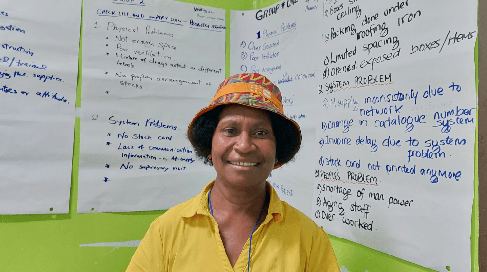 Woman in yellow shirt stands in front of series of flip charts on supply chain issues.