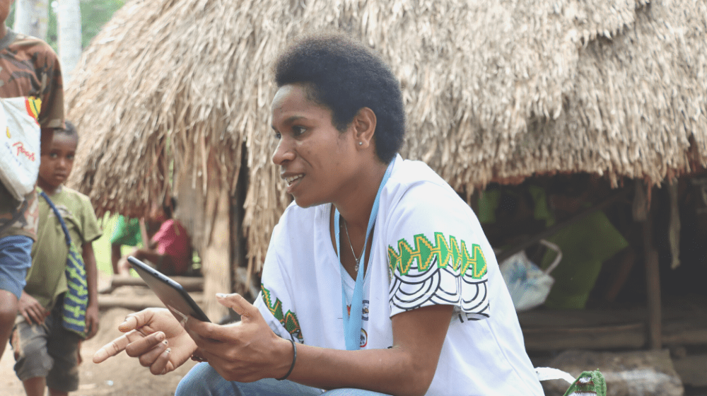 Woman with tablet sits in front of small house.