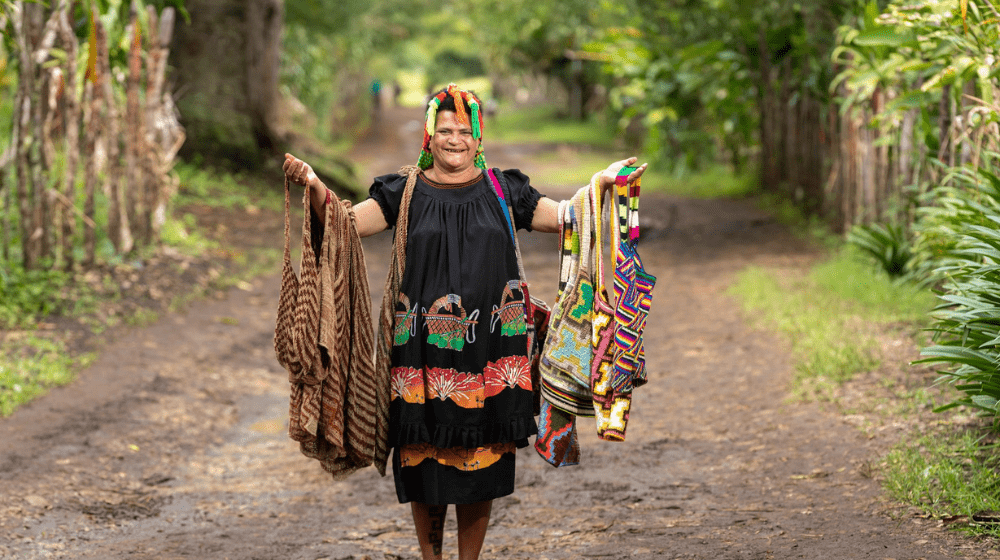 Woman holding several bilums with arms outstretched in rural laneway.