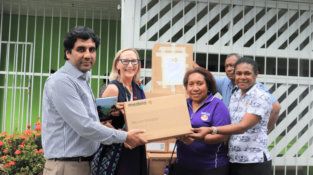 Four people hold cardboard box in from of Port Moresby General Hospital.