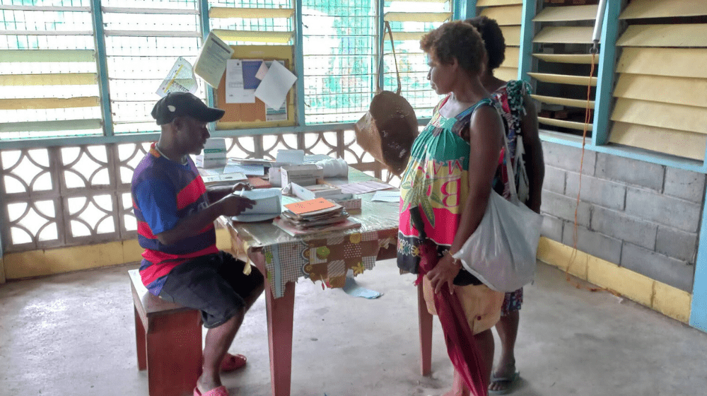 Man sits while pregnant woman is standing at check-in for antenatal clinic.