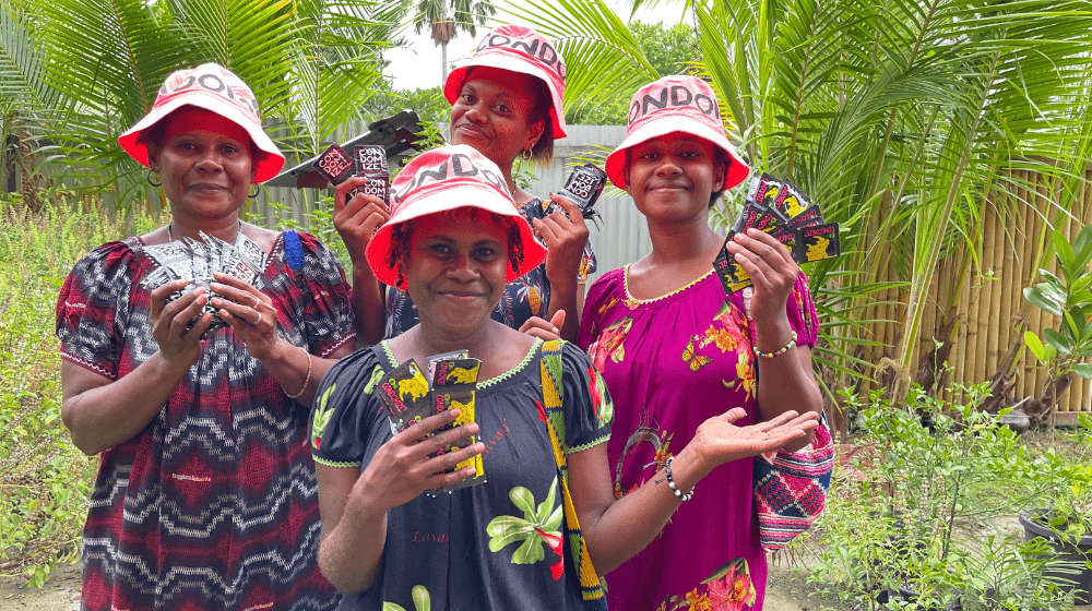 Four women in bright pick hats holding condoms up to the camera.