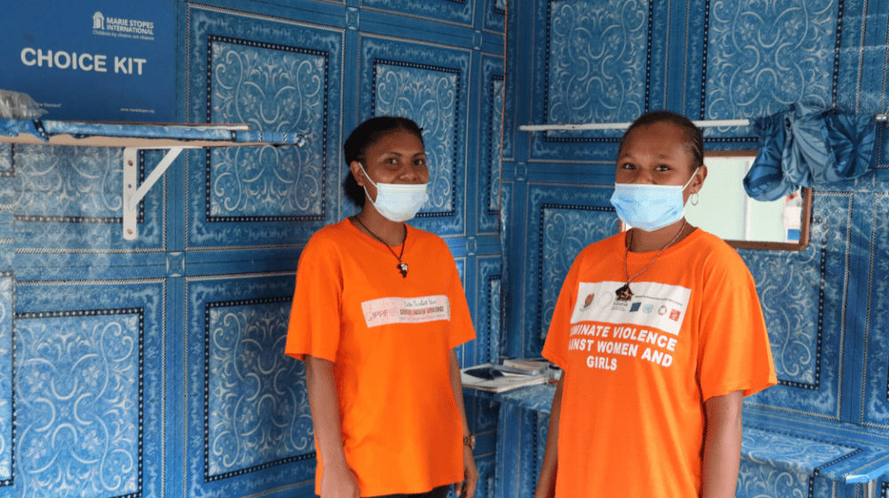 Two women in orange t-shirts are in clinic space.