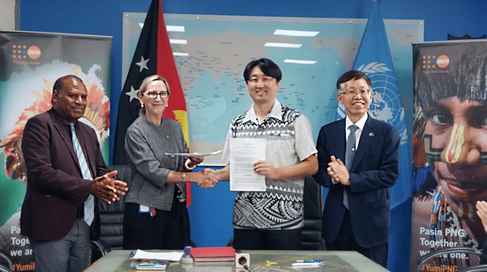 Four people standing facing camera with two holding paper for grant agreement.