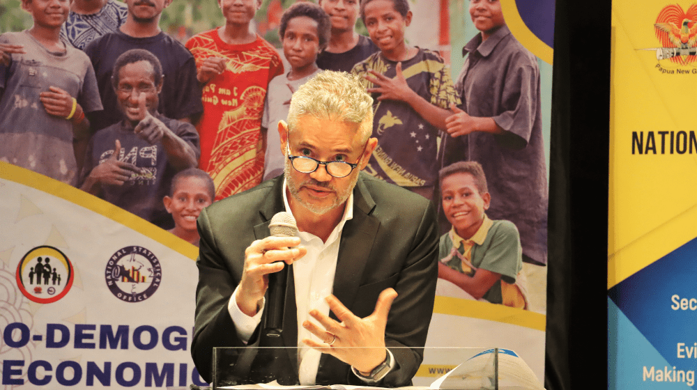 Man speaks behind lectern with standing banners behind.