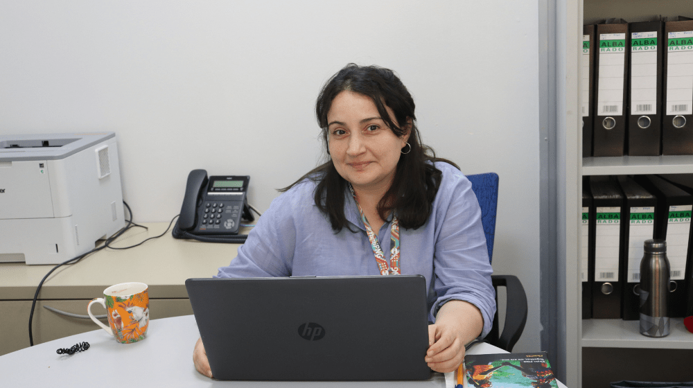 Woman in blue shirt sits at desk with laptop