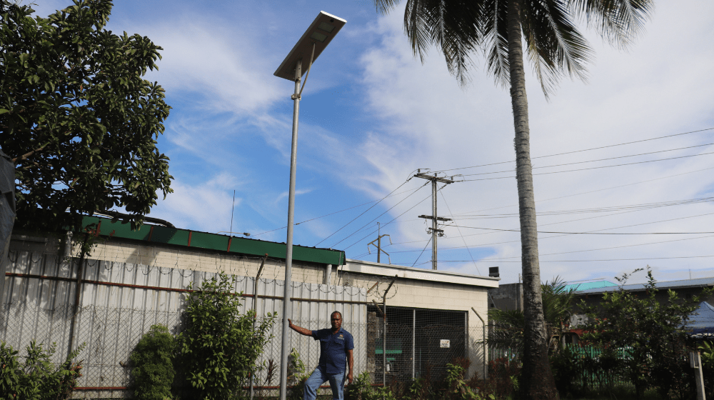 Man standing next to light pole with solar panel on top. 