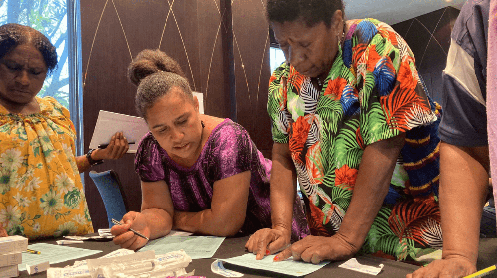 Three women around a table calculating stock levels.