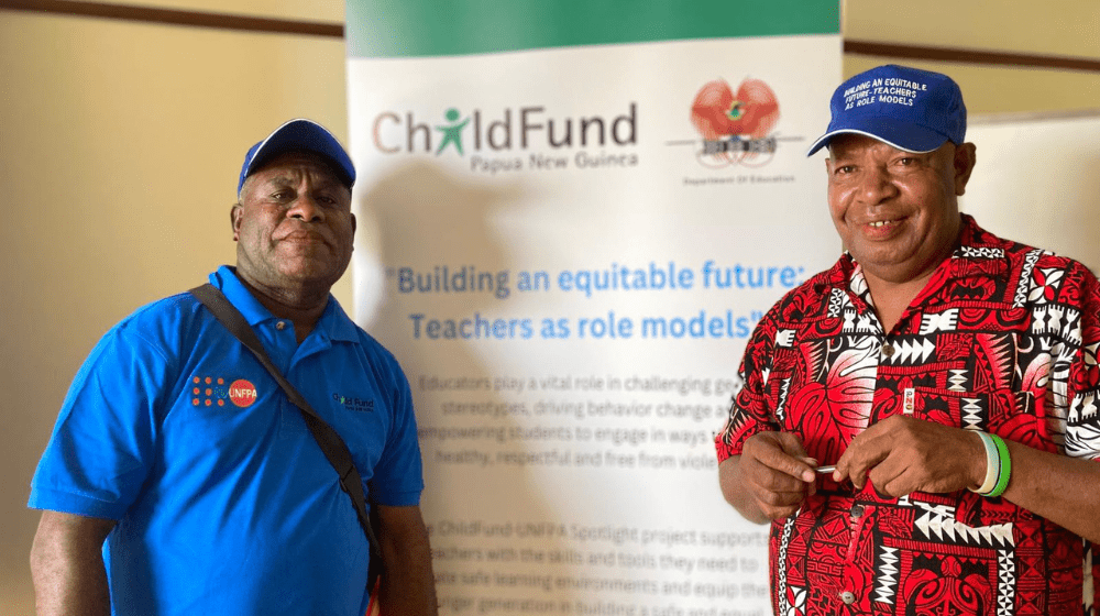 Two men standing and looking to camera in front of banner.