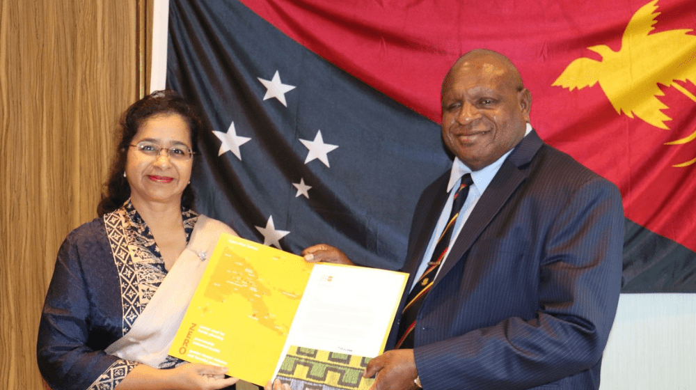 Woman and man holding folder with Papua New Guinea flag in background,