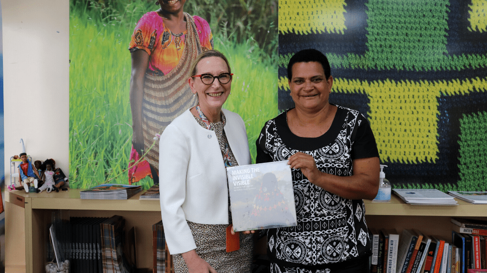 Two women stand showing book on bilum patterns.