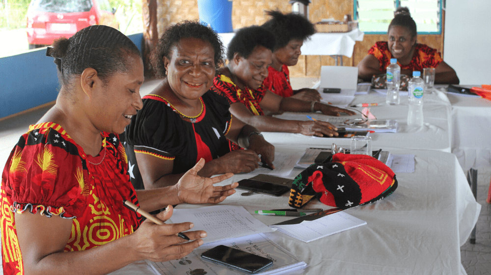 Two women sit at a table with pens, paper, and worksheets during workshop.