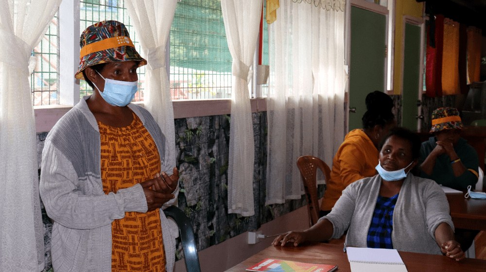 Woman in orange t-shirt speaks before a group of workshop participants