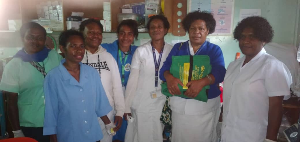 Seven women health workers in hospital office. One holds the anti-shock garment.
